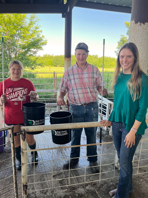 2024 Summer Intern, Regan Ast, poses with members of the 4-H community while handing out buckets at the Hodgeman County Fair.