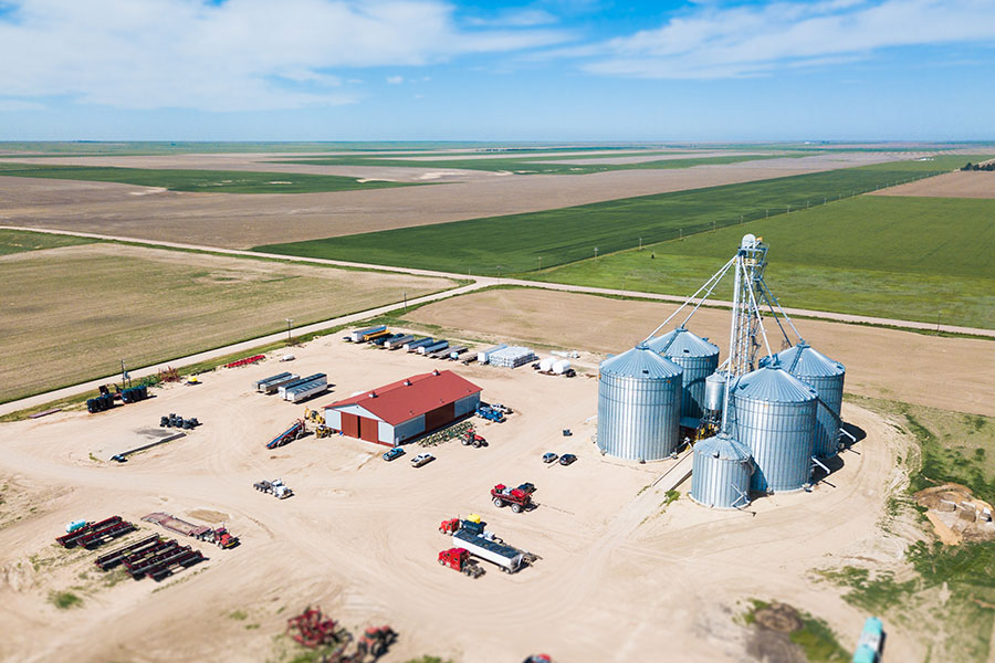 Aerial Farm Operation Aerial view of a large farm with storage silos, farming equipment, and expansive agricultural fields under a clear sky.