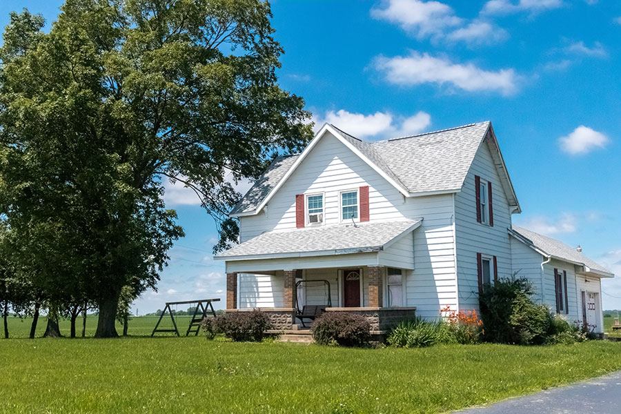 A farmhouse with a large front yard and trees under a clear blue sky, showcasing rural agricultural property.
