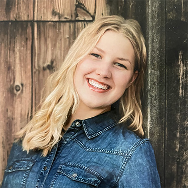 Outdoor photo of Allyson Rietcheck leaning against an old wood barn door.