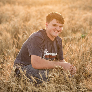 Outdoor photo of James Seeman kneeling in a wheat field.