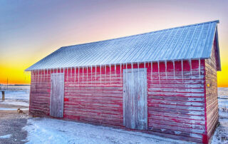 Q1 2026 Calendar Photo Contest Winner. Old red shed with long icicles hanging from the eaves against a frosty winter sunset. Submitted by Grant Pfannenstiel.