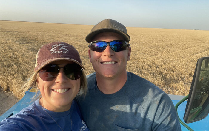Lindy McMillen and her husband take a selfie in front of a wheat field that is ready to be harvested.